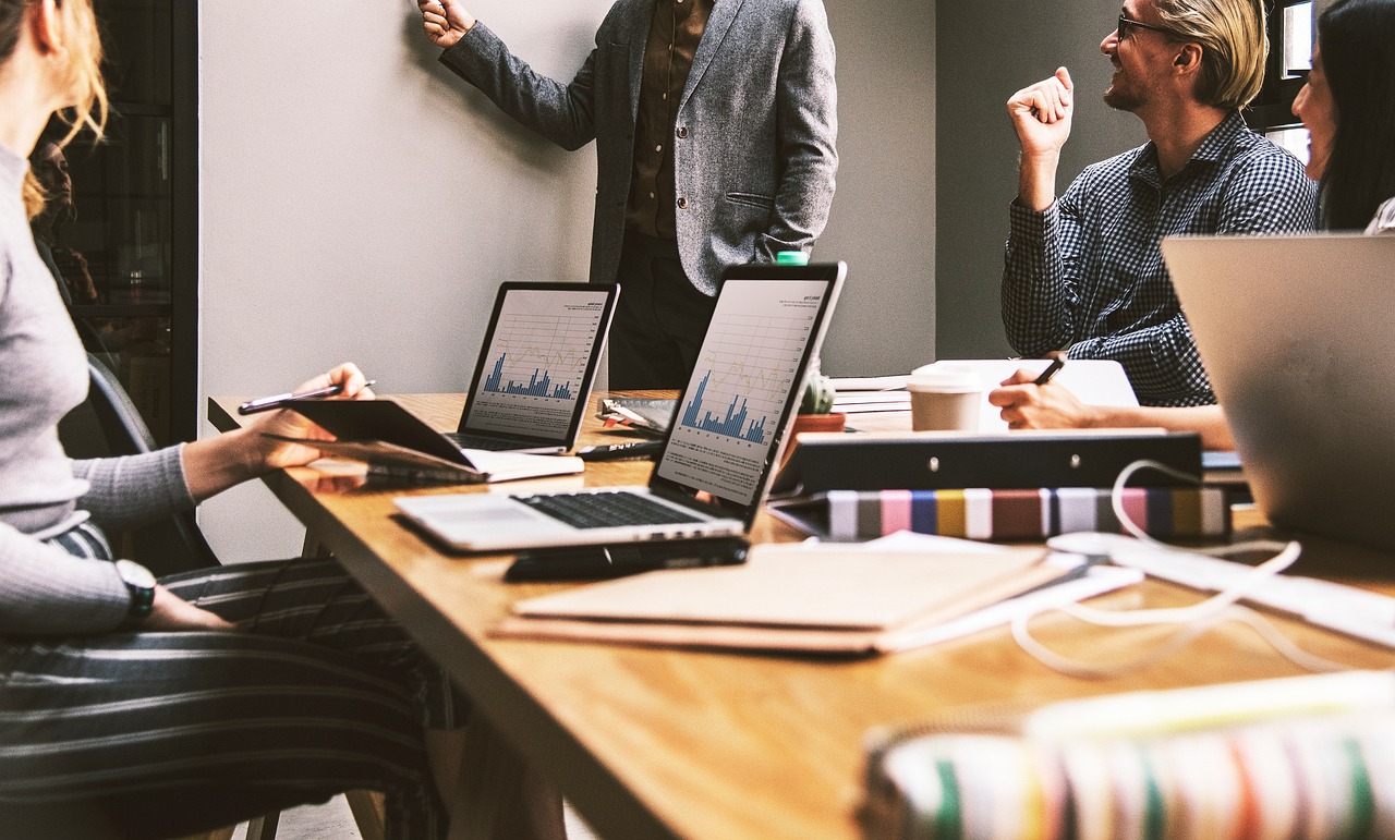 Laptops and paperwork on a conference table while an employee is presenting to their team.